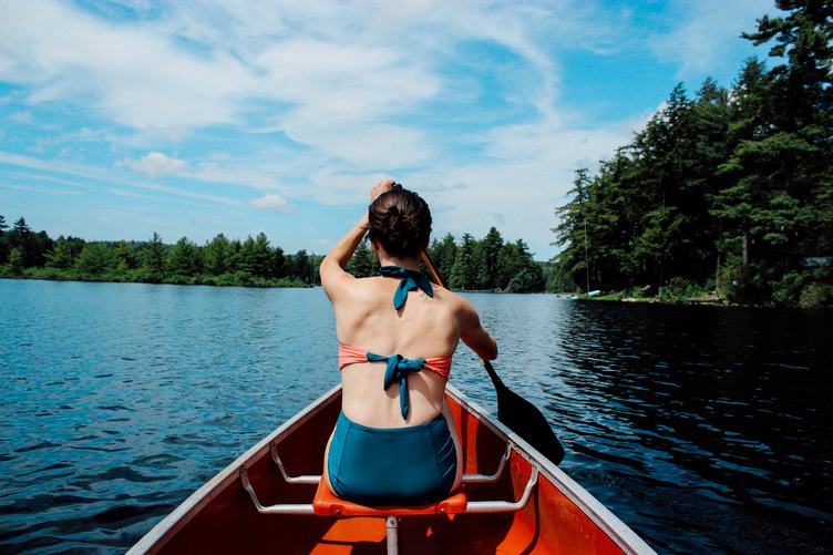 Young Brunette Girl Wearing Bikini and Sitting in a Kayak on a Lake