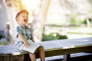 Boy Sitting on Bench and Laughing Against Light Blurry Background