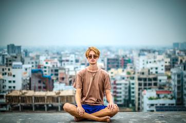 Young Barefoot Man Sitting on Roof Against Blurry City Space