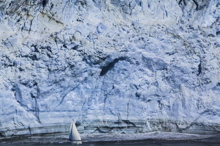 Small Sailboat against a Huge Blue Iceberg
