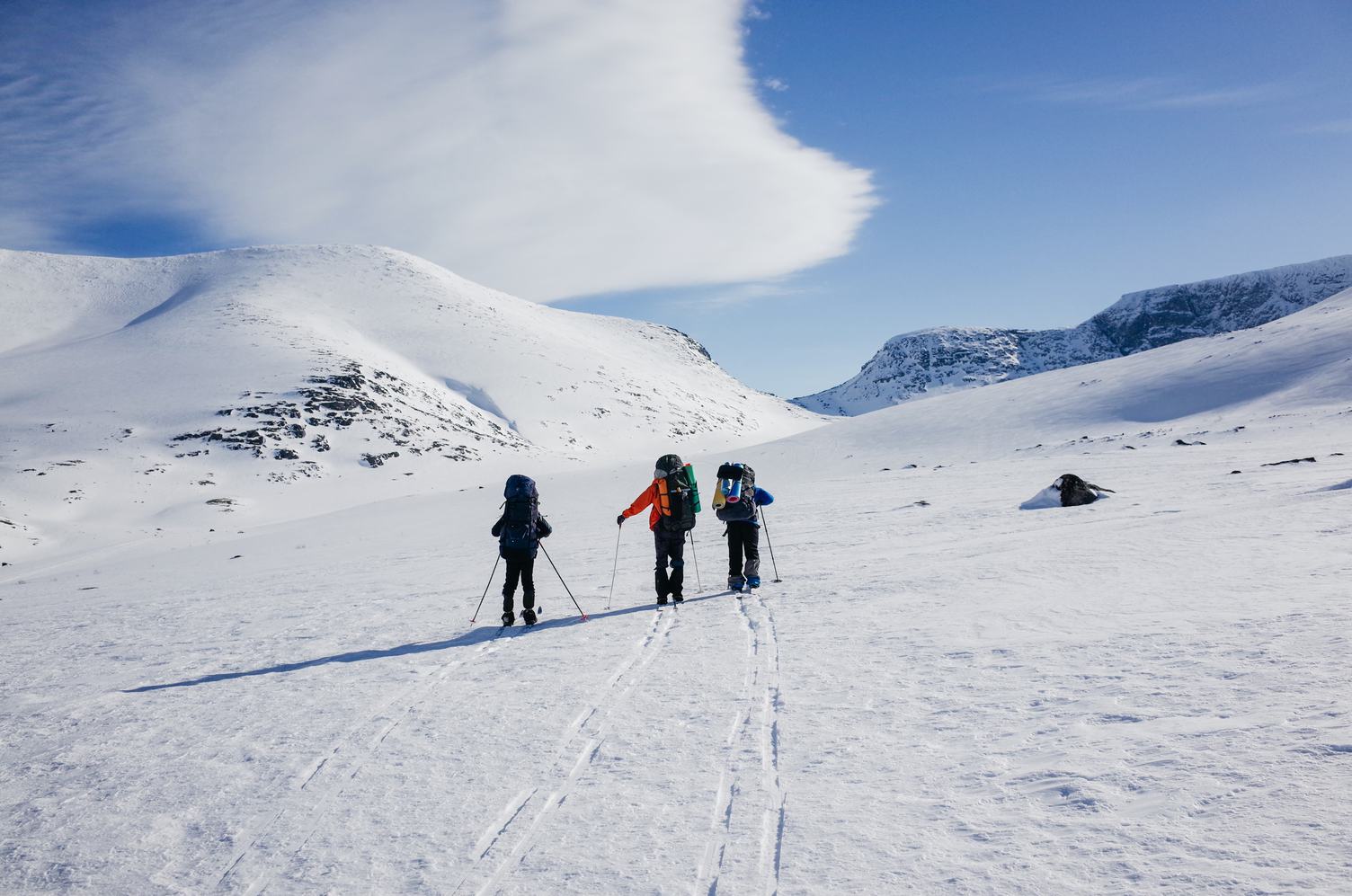 Three People Walking over Snowy Valley with Backpacks