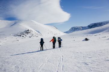 Three People Walking over Snowy Valley with Backpacks
