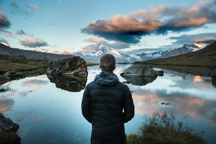 Man Standing and Looking on Peaks Reflecting in Mountain Lake