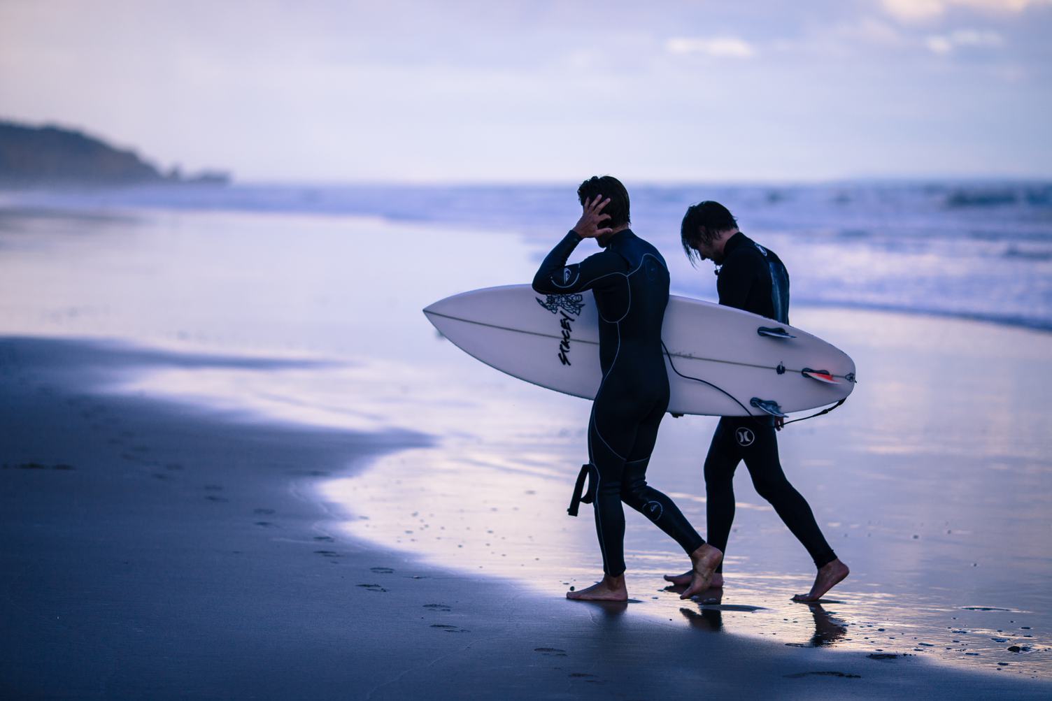 Two Men Carrying Surfing Board at the End of Day