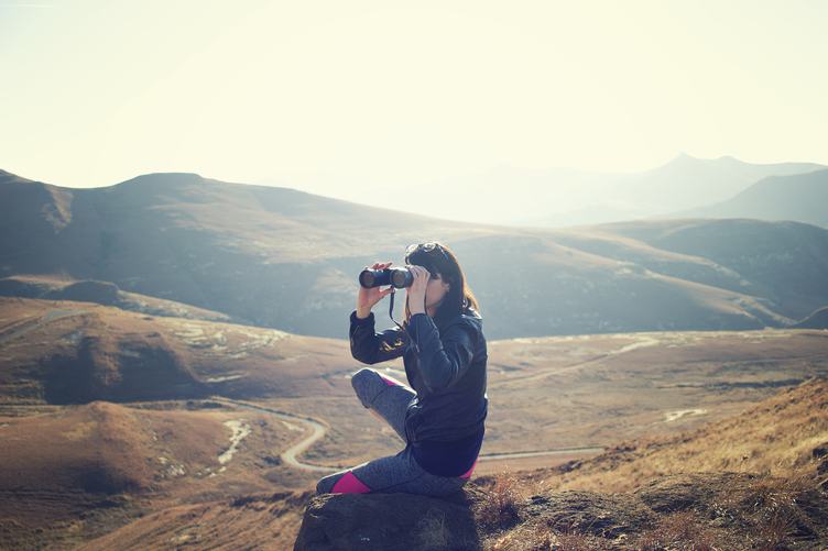 Girl Looking through Binoculars in the Mountains