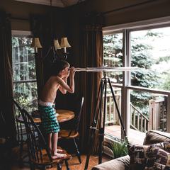A Young Boy Observing the Nature Through a Telescope from Indoors