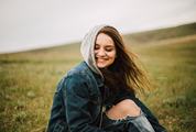 Smiling Long-hair Girl in a Hood Sitting in the Meadow