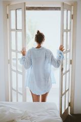 Young Woman in a Shirt Opening the Balcony Door