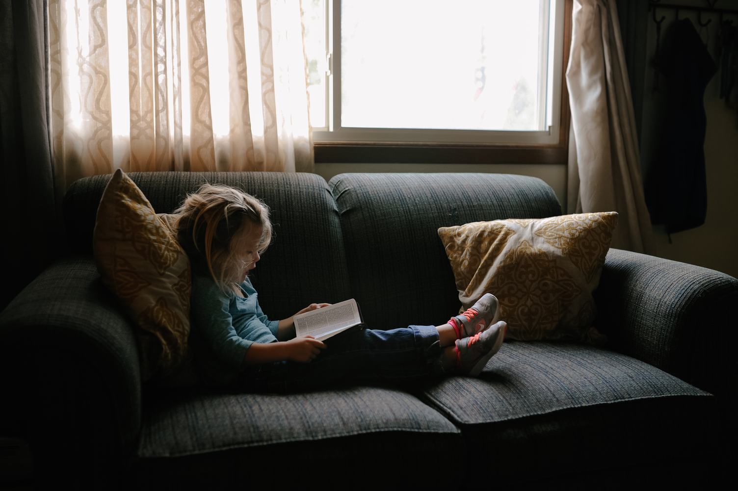 Young Girl Reading a Book and Sitting on Sofa at Home