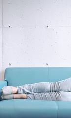 Legs of Young Woman Lying on Blue Sofa against Concrete Wall