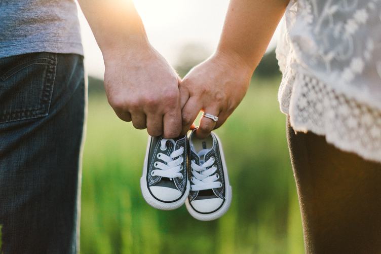 Future Parents Holding Hands and a Pair of Little Baby Shoes