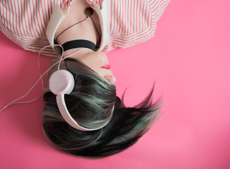 Young Girl Listen to Music Lying on Pink Background