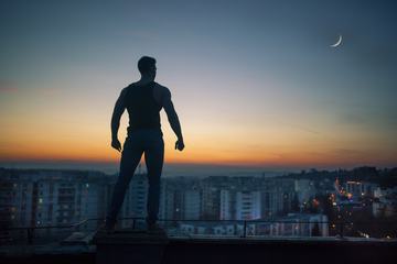 Brave, Young and Muscular Man Standing on the Roof Looking Far Away at Sunset