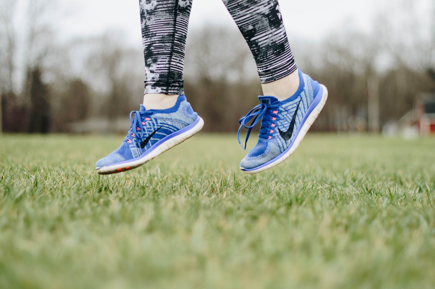 Closeup of Female Legs Wearing Blue Sneakers Jumping on the Grass Outdoors