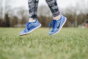 Closeup of Female Legs Wearing Blue Sneakers Jumping on the Grass Outdoors