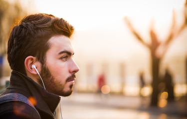 Young Man with In-ear Headphones Portrait in Profile Outdoors