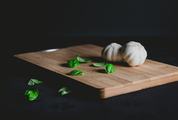 Wooden Chopping Board with Garlic and Basil Leaves on Black Background