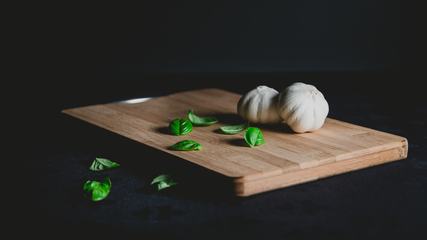 Wooden Chopping Board with Garlic and Basil Leaves on Black Background