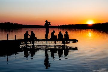 Silhouette of Group of Friends Sitting and Drinking on a Lake Pier at Sunset