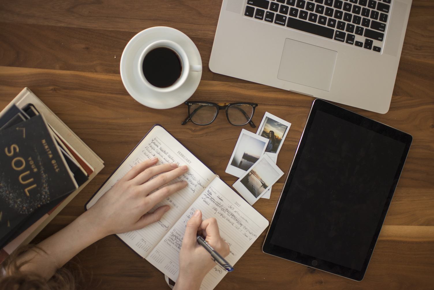 Top View of Hand Writing on a Notebook, with Laptop, Tablet and Hot Coffee