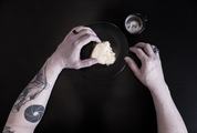 Close up of a Tattooed Man's Arms Eating Breakfast against Black Background