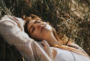 Young Woman Relaxing Lying on the Grass with Closed Eyes Enjoying Sunlight