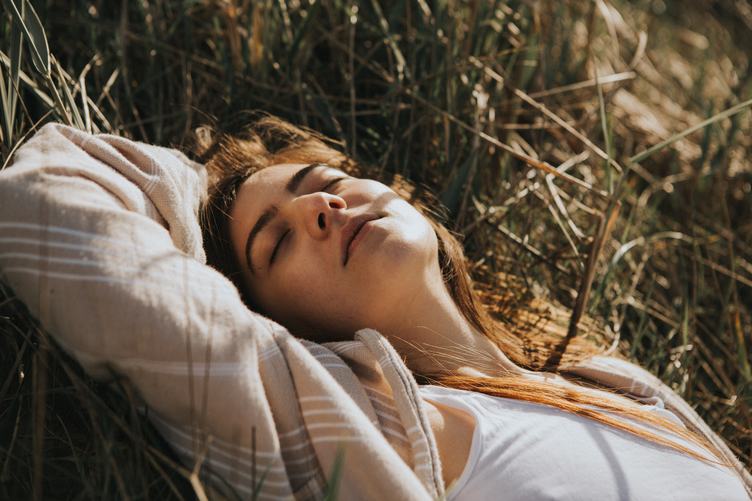 Young Woman Relaxing Lying on the Grass with Closed Eyes Enjoying Sunlight