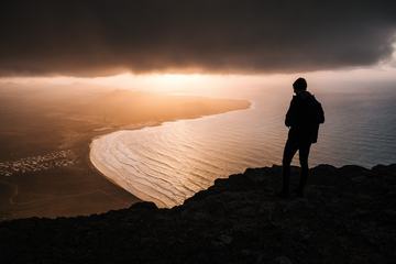 Man Silhouette High on Cliff at Sunset