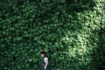 A Little Girl Standing and Laughing against Green Leaves Wall