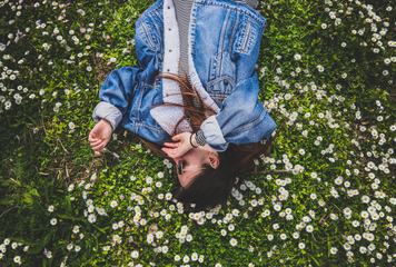 Young Brunette Enjoying Lying on the Grass full of Daisies