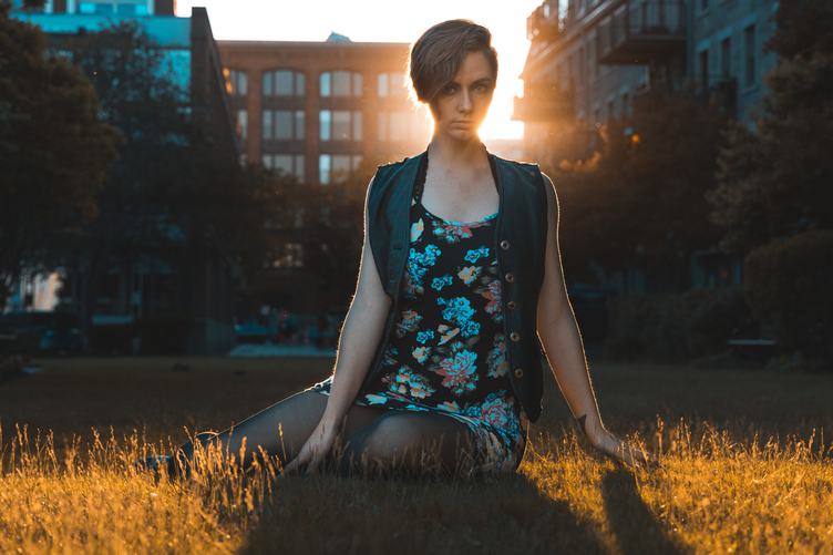 Young Pretty Woman Sitting on the Grass at Sunset