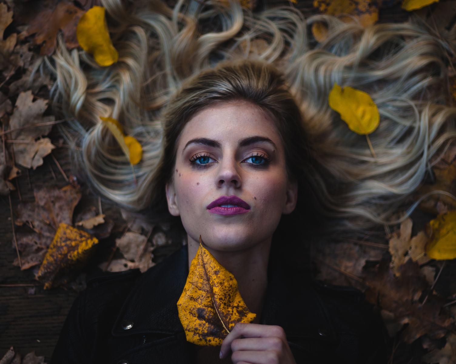 Beautifu Woman with Pink Lips Lying on Autumn Leaves