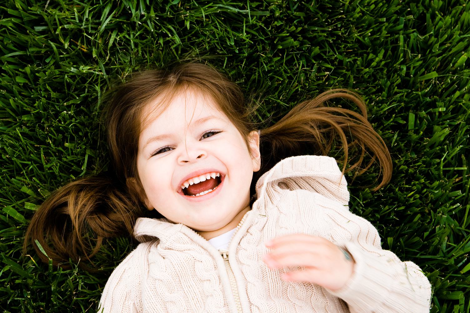 Portrait of a Laughing Little Girl Lying on Green Grass