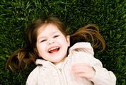 Portrait of a Laughing Little Girl Lying on Green Grass