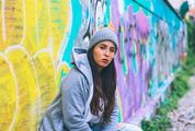 Young Woman Wearing Tracksuit and Glasses Sitting against Graffiti Wall