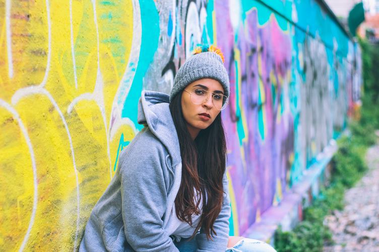 Young Woman Wearing Tracksuit and Glasses Sitting against Graffiti Wall