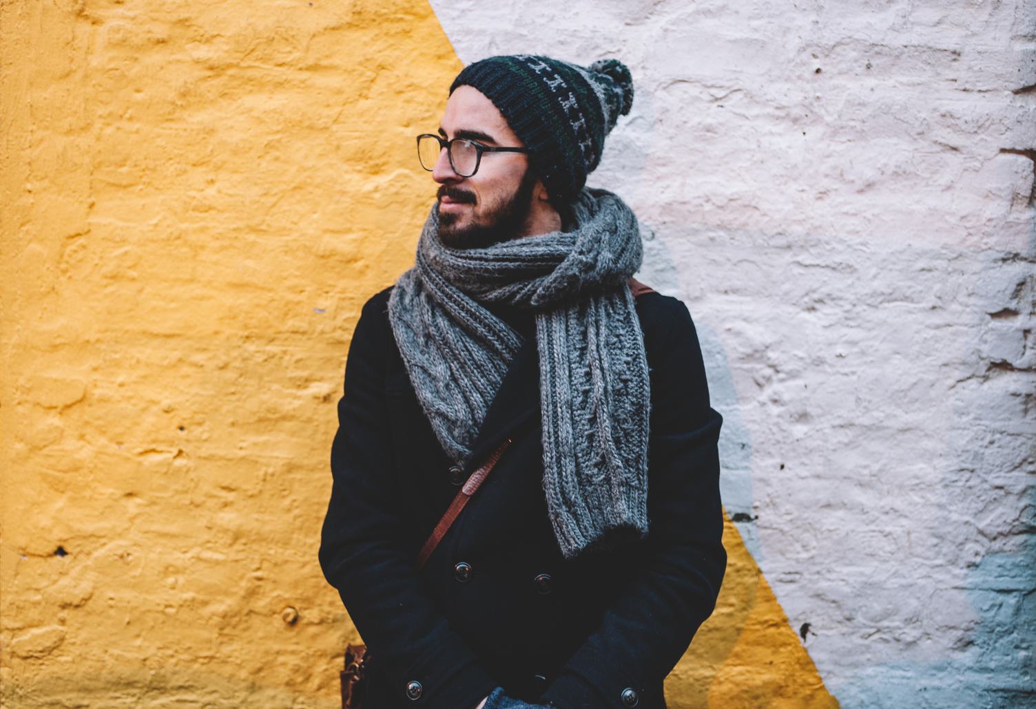 Young Male Wearing Coat, Hat and Scarf against Brick Wall