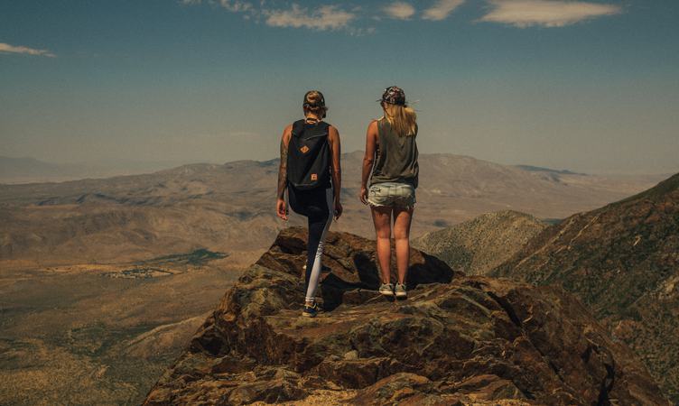 Two Girls Standing Back on Top of a Mountain Enjoying the View