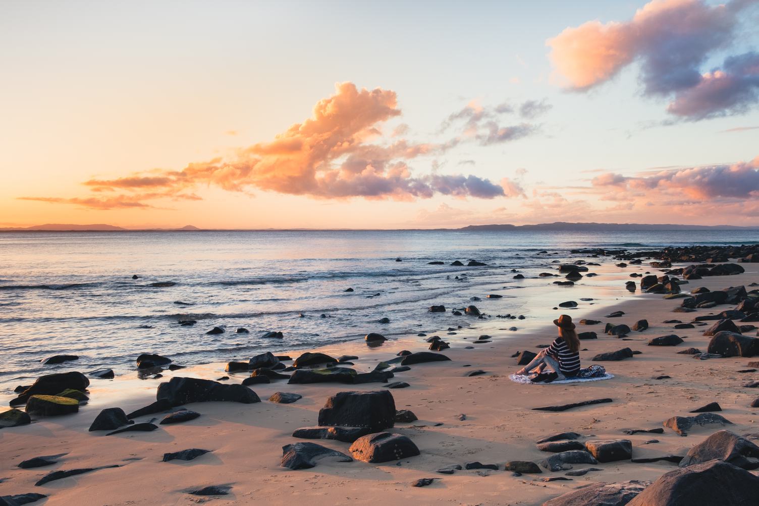 Woman in a Hat Sitting on the Beach and Admiring the Sunset