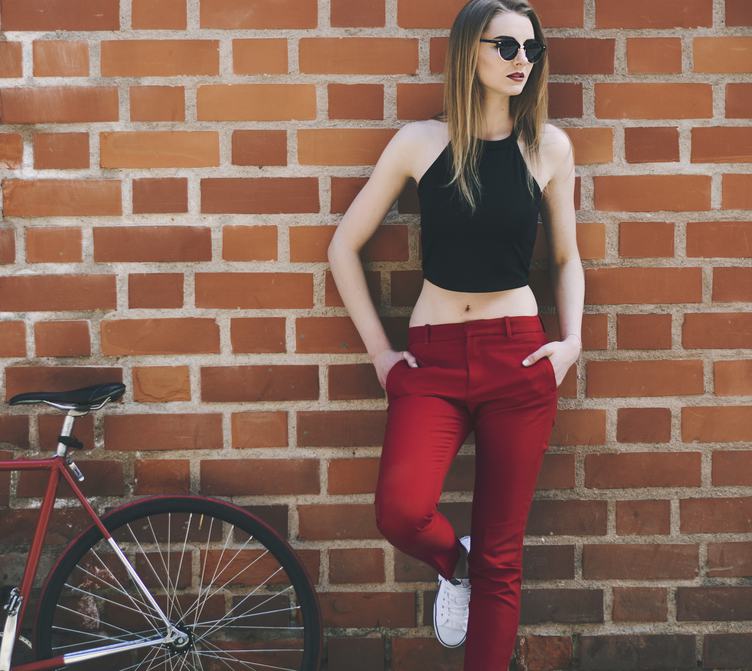 Young Woman with Her Bike Leaning against Red Brick Wall