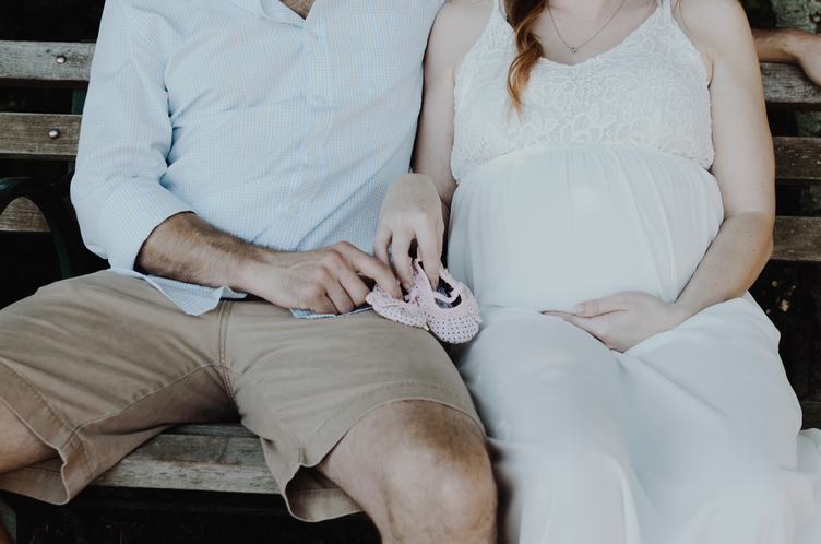 Couple Future Parents Sitting on the Bench Holding Tiny Crochet Boots