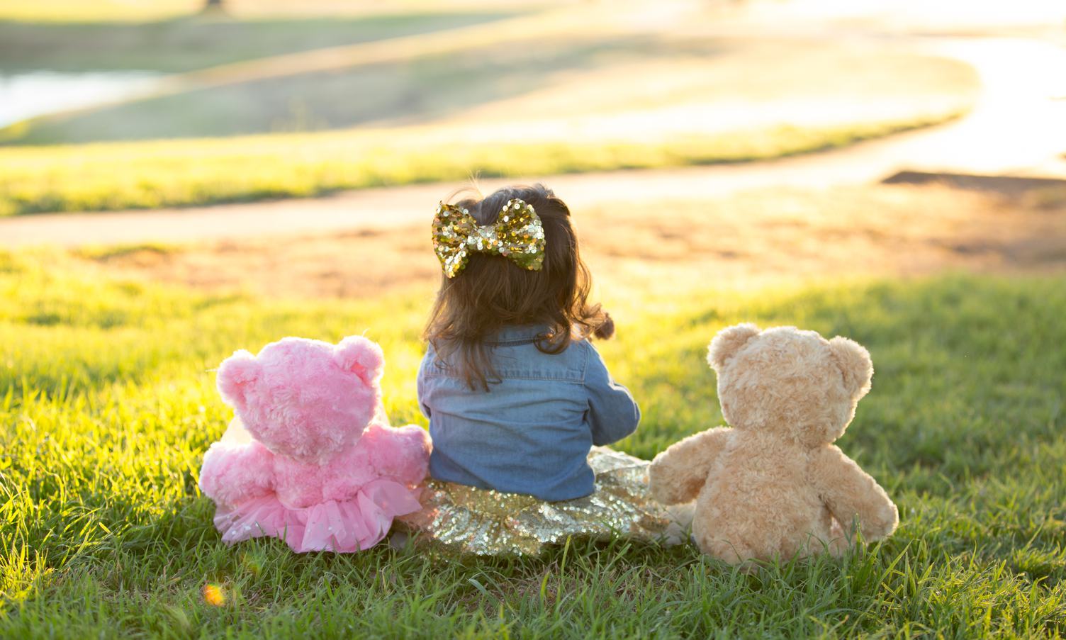 Little Girl Sitting on the Grass with Her Teddy Bears