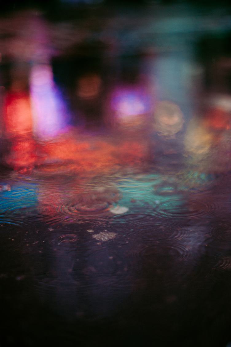 A Puddle Reflects Colorful Lights at Night During a Rain