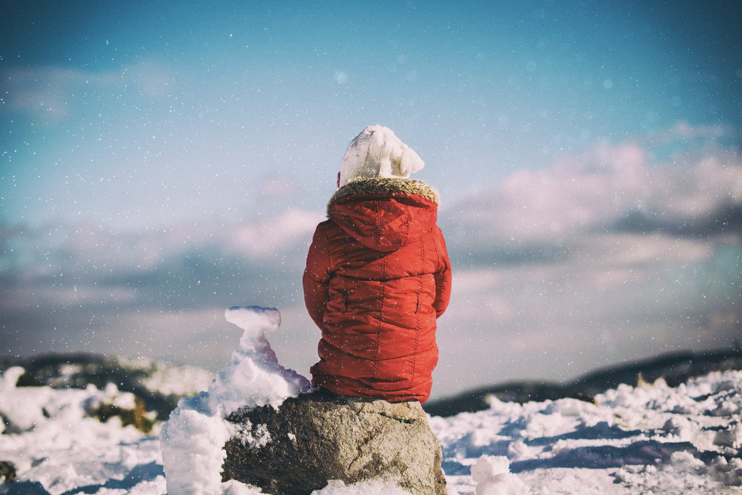 Child Sitting on the Rock when It Is Snowing