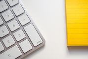 Keyboard and Yellow Notepad on a White Desk