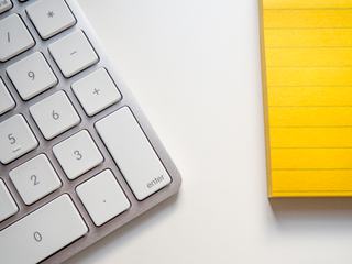 Keyboard and Yellow Notepad on a White Desk