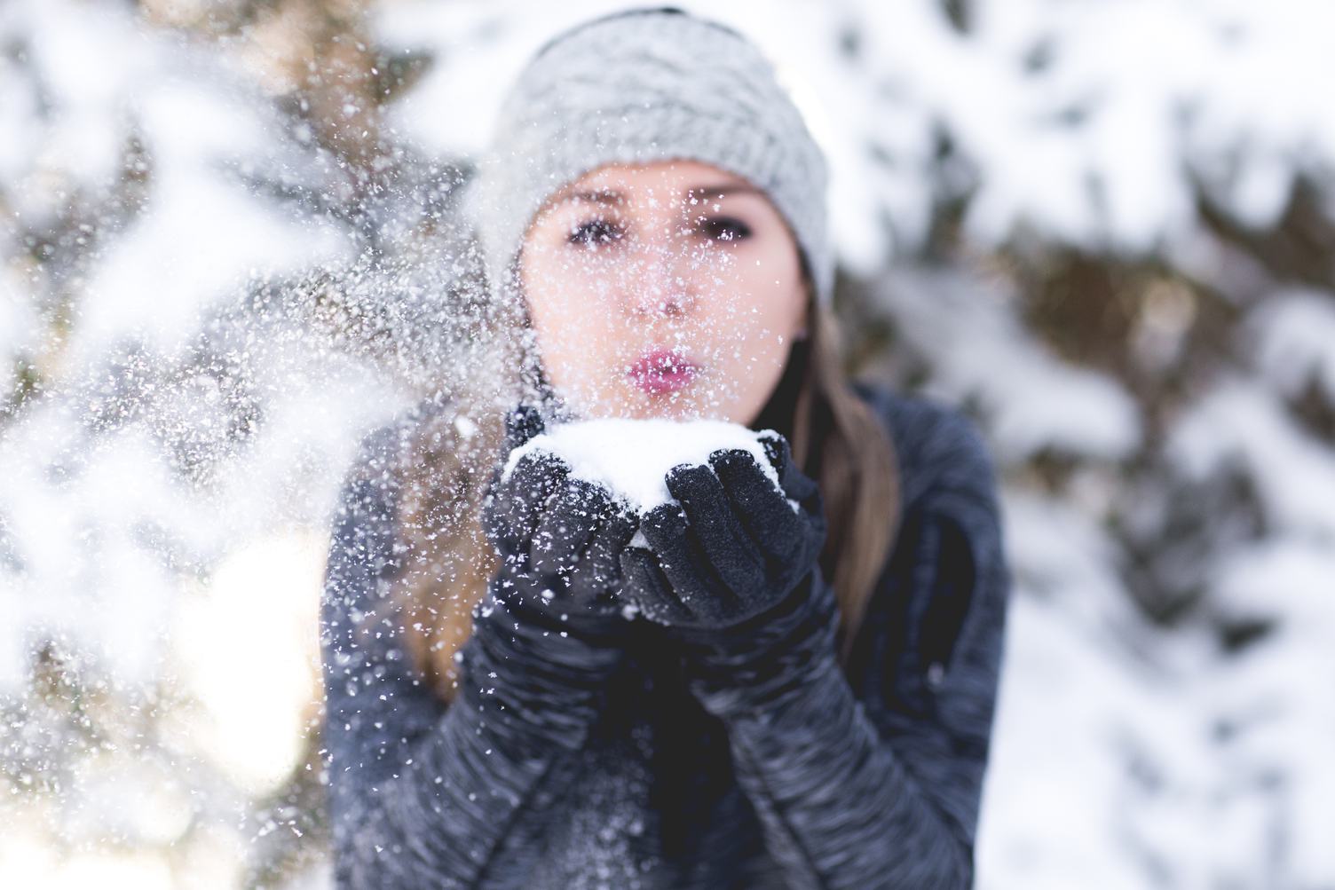 Young Woman Blowing Snow toward Camera Outdoors